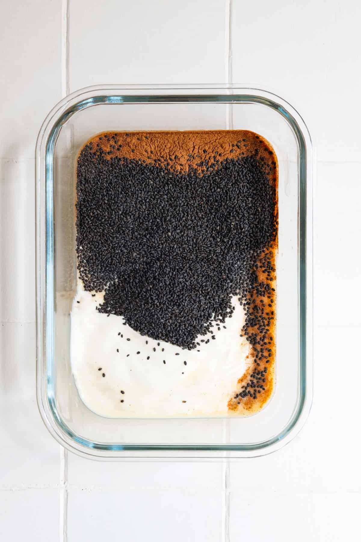 Basil seeds, nondairy milk, date syrup, cinnamon, yogurt, and vanilla in a glass container.