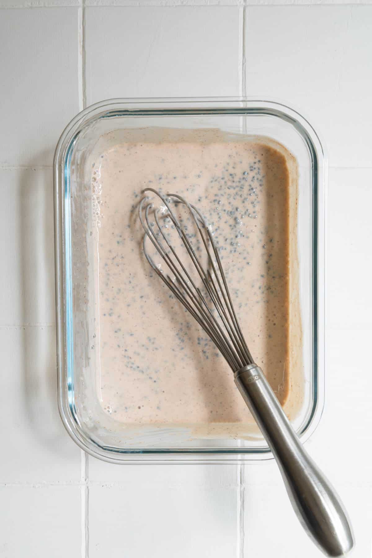 Yogurt, seeds, nondairy milk, cinnamon, and vanilla with a whisk in a glass dish.