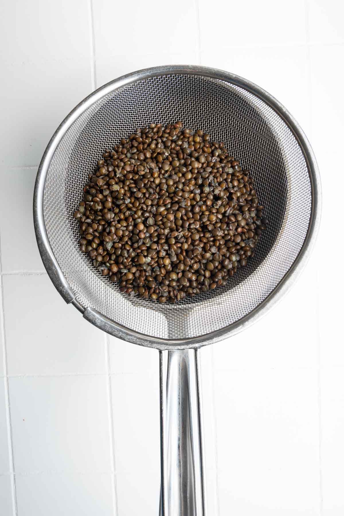Cooked black lentils in a mesh sieve.