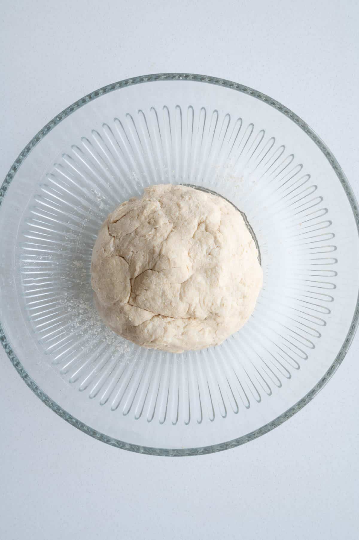 A rolled ball of dough in a glass bowl.