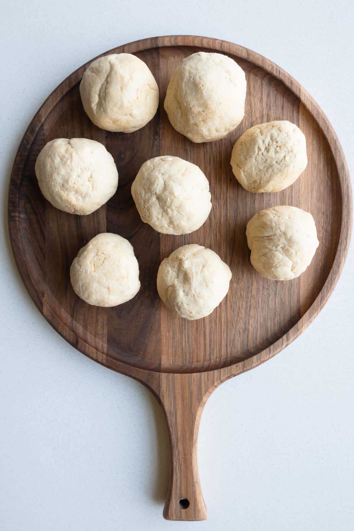 Eight dough balls on a wooden cutting board.