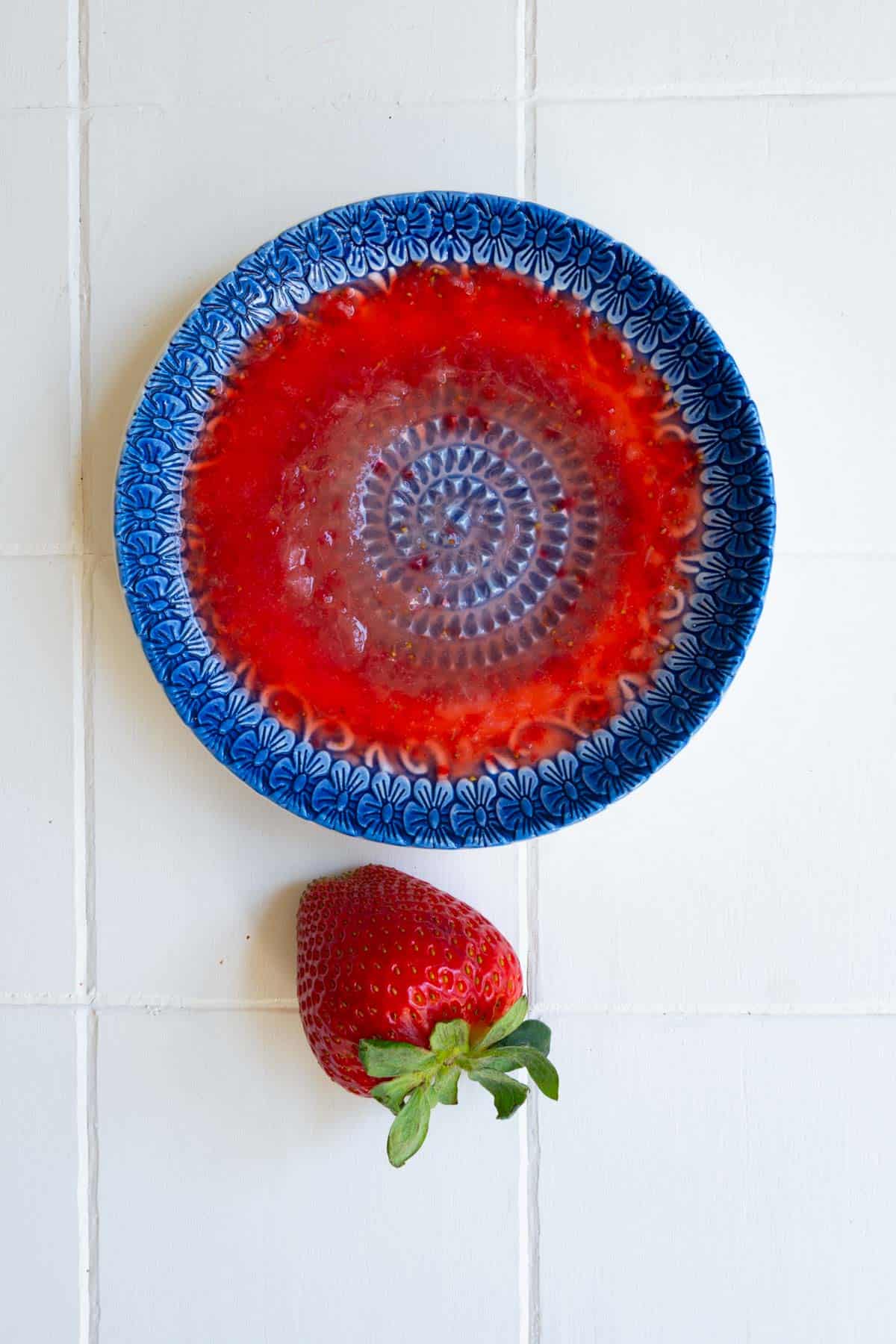 A ceramic garlic grater plate with mashed strawberry around the edges.