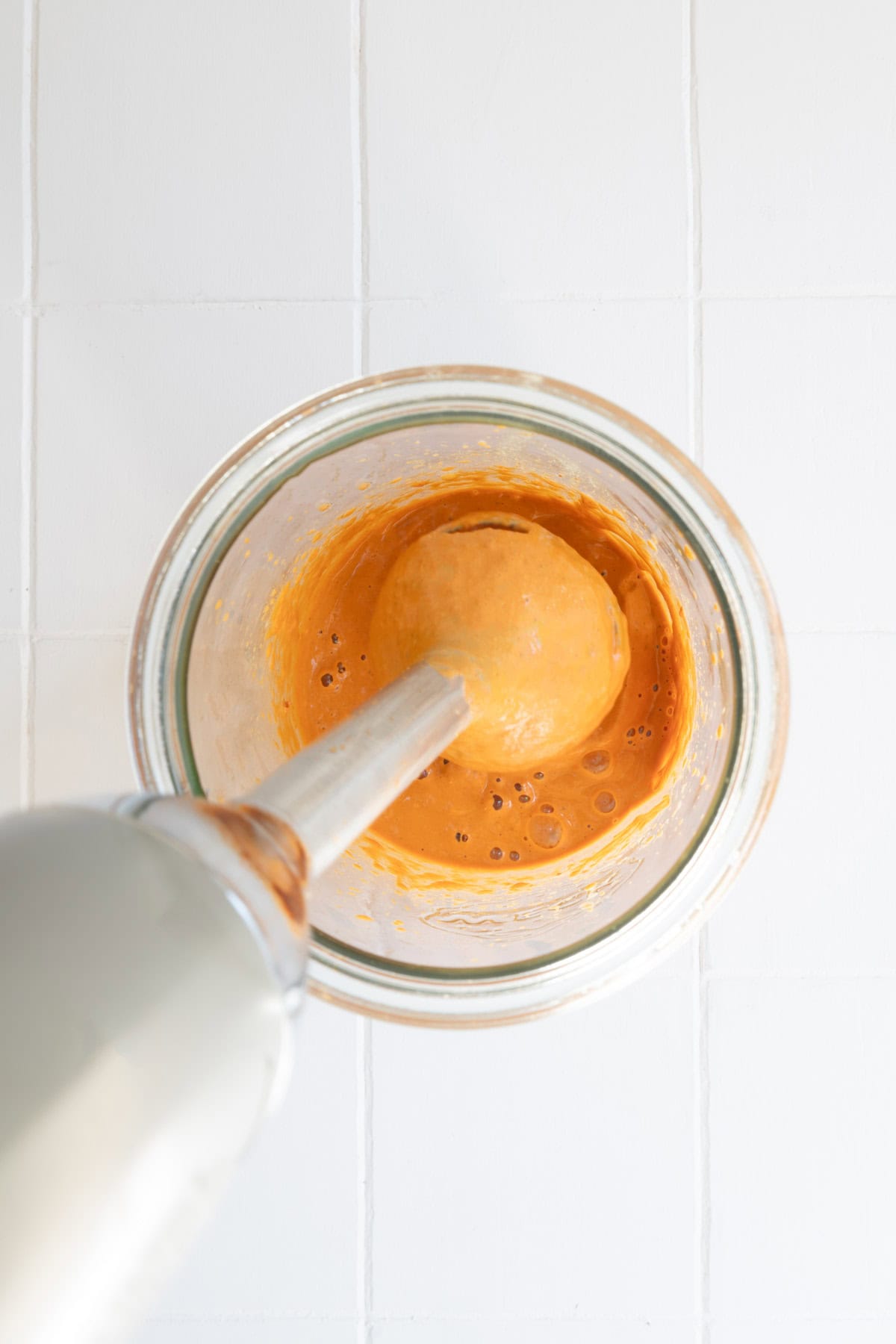 Immersion blender with orange creamy dressing in a jar.