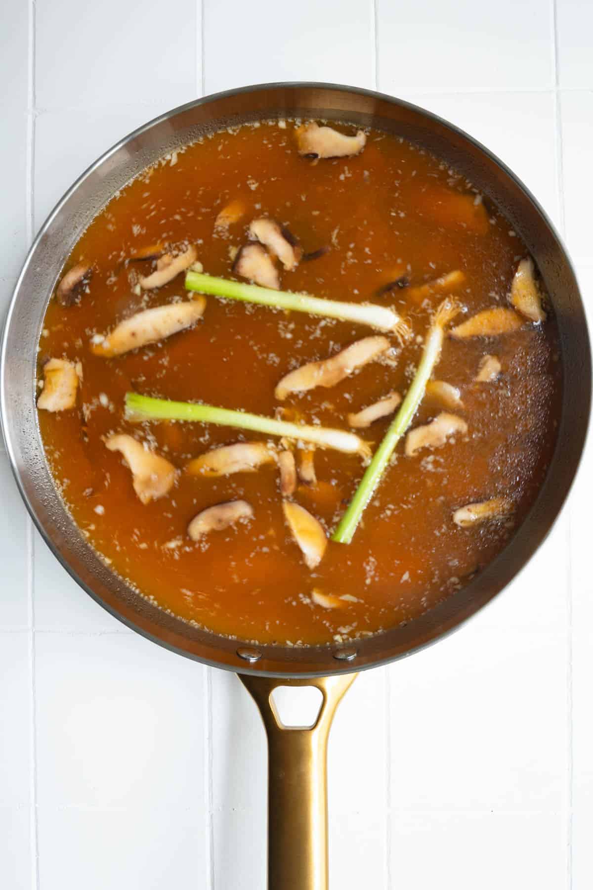 Vegetable broth, garlic, ginger, tamari, miso, mushrooms, and green onion in a skillet.