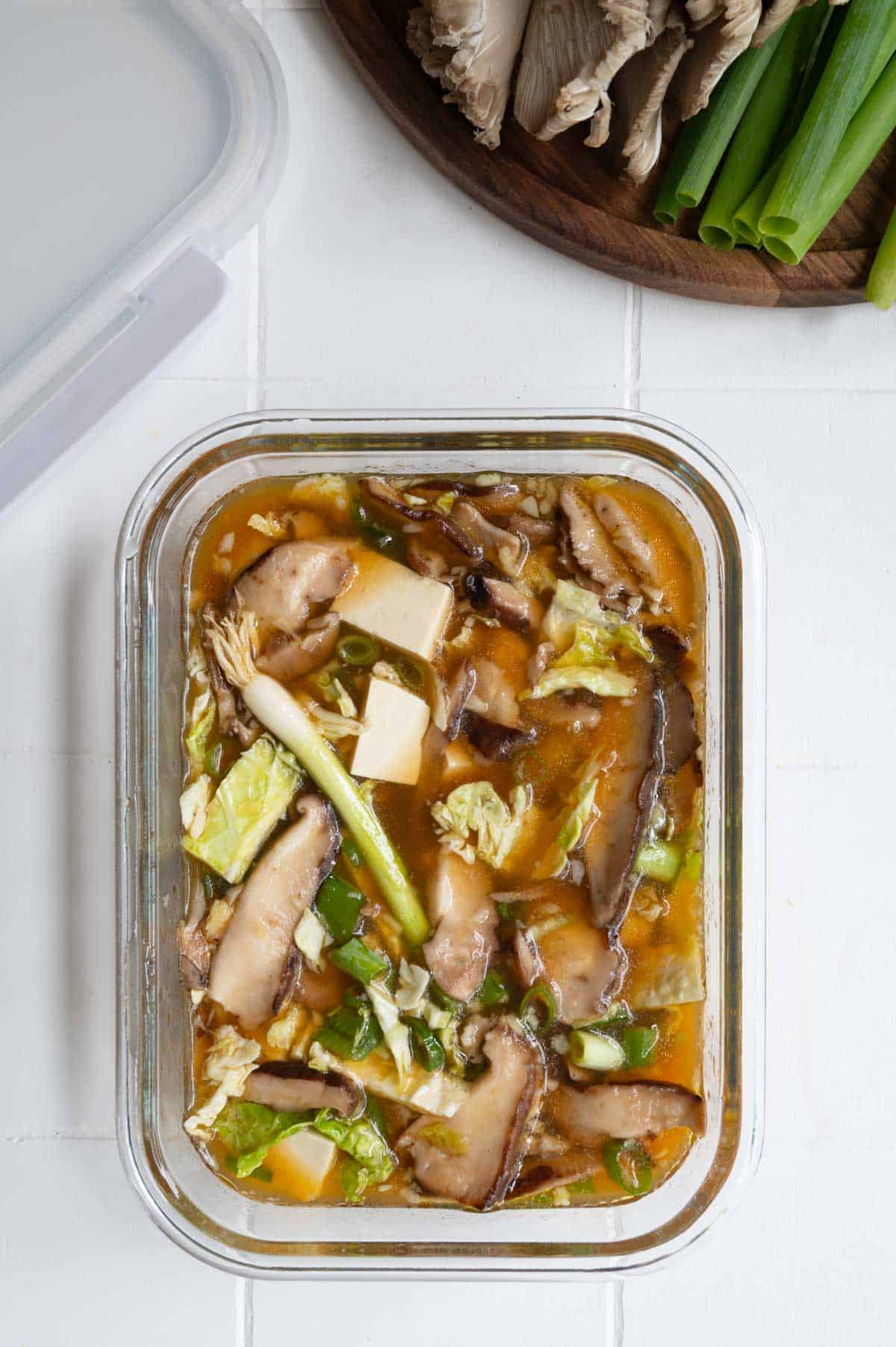 Broth, tofu, shiitake, cabbage. green onion, and aromatics in a glass container.