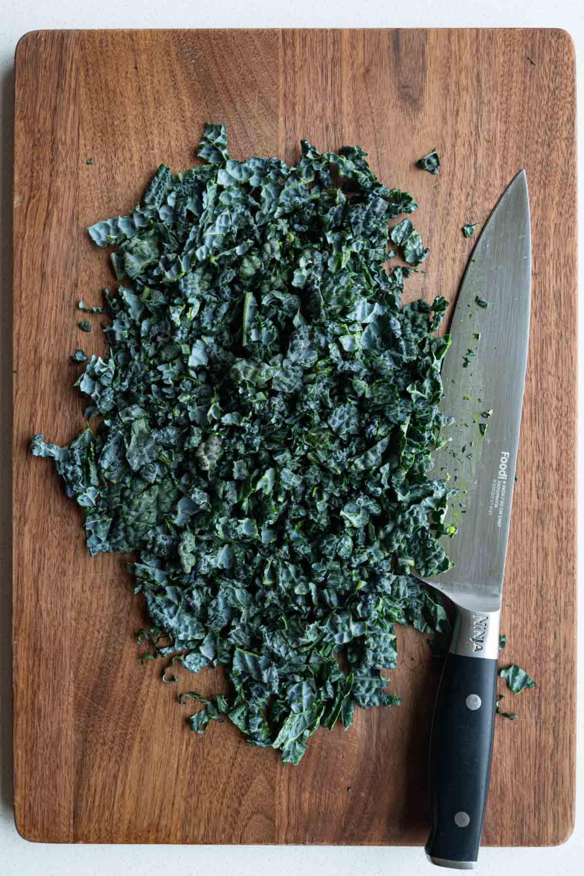 Chopped lacinato kale on a wooden cutting board with a chef's knife.