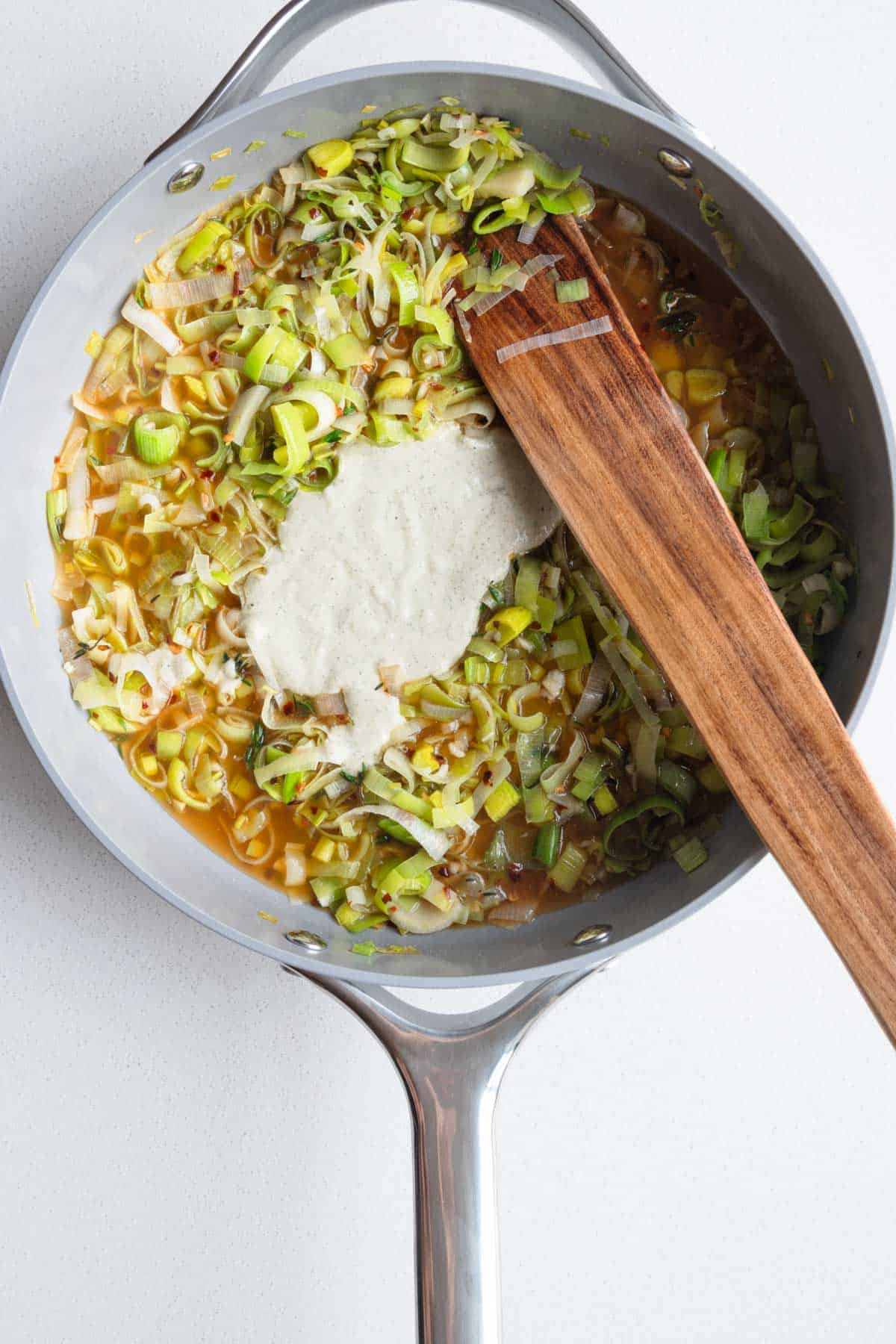 Cooked leek in broth with nondairy cream in a skillet.