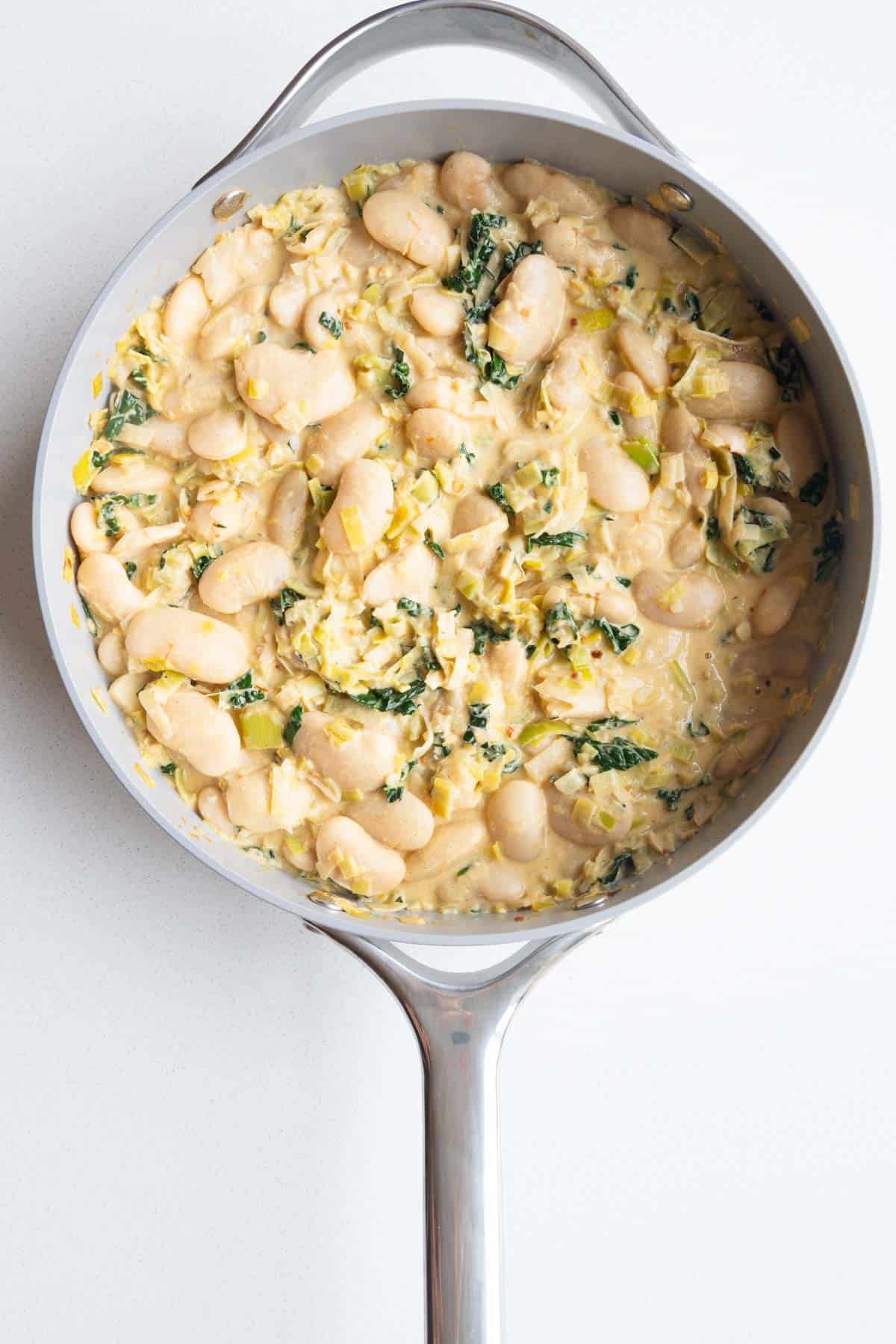 White beans cooking in a creamy dairy-free sauce.