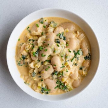 Creamy gigante beans with leek in a white bowl.