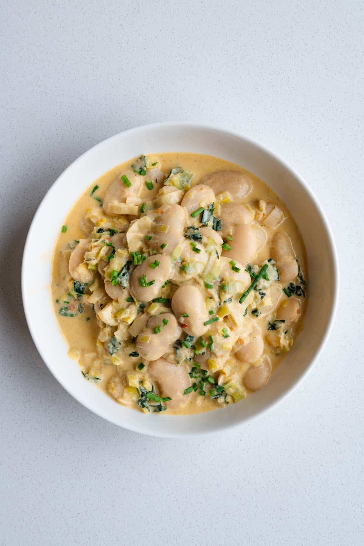 Creamy gigantes with leeks in a white bowl.