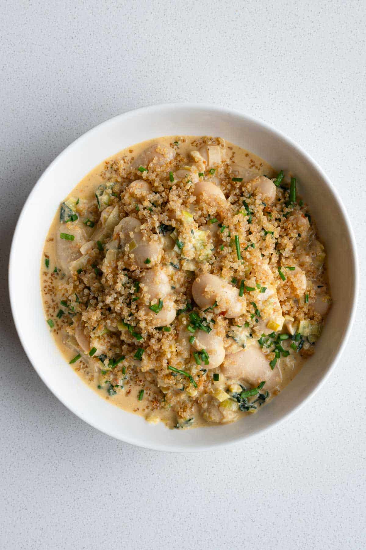 Creamy gigante beans with leek topped with crispy quinoa and chopped chives in a white bowl.