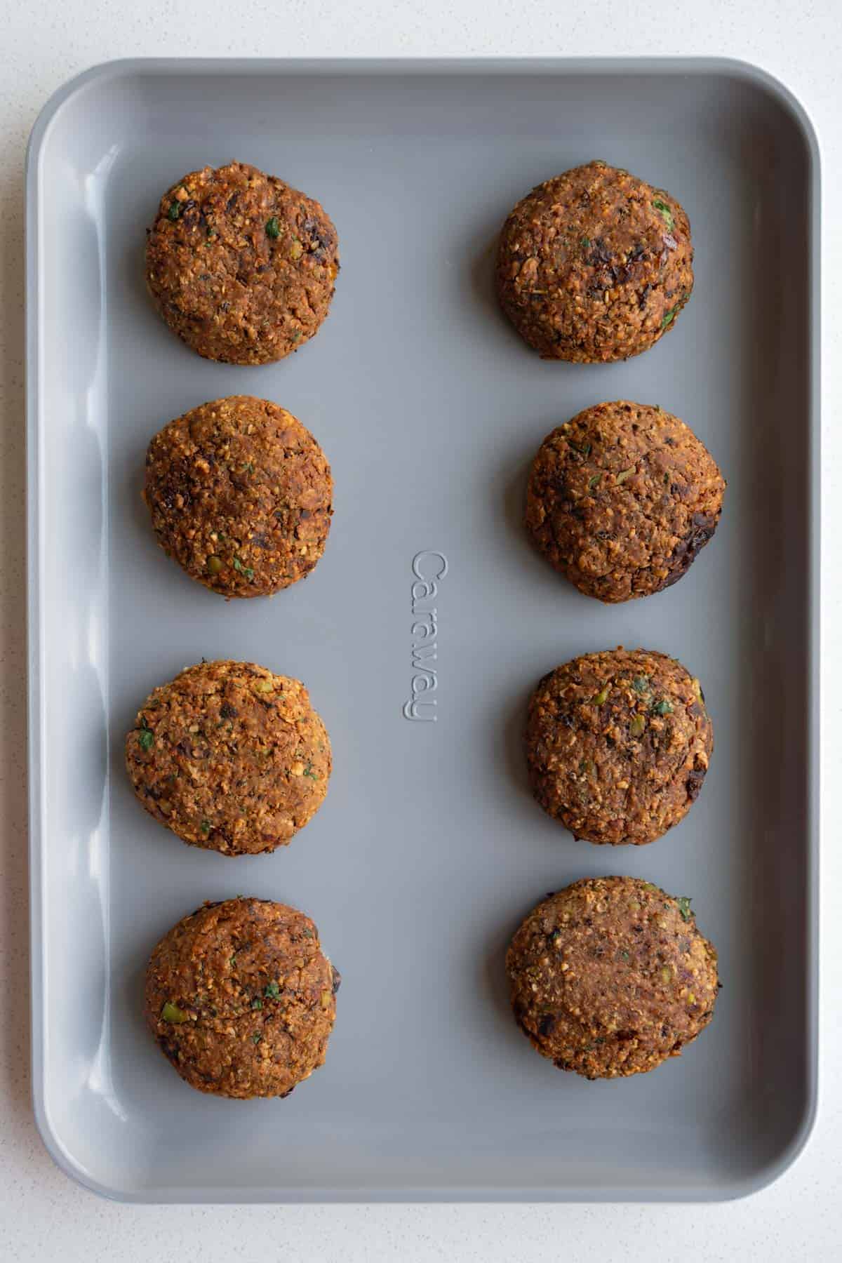 Eight baked edamame black bean burgers on a baking sheet.
