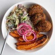 Edamame black bean burgers with pickled red onion, sweet potatoes, and creamy coleslaw in a bowl.