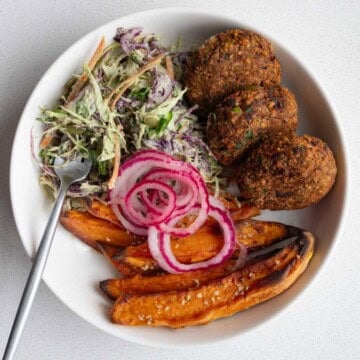 Edamame black bean burgers with pickled red onion, sweet potatoes, and creamy coleslaw in a bowl.