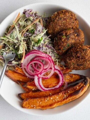 Edamame black bean burgers with pickled red onion, sweet potatoes, and creamy coleslaw in a bowl.
