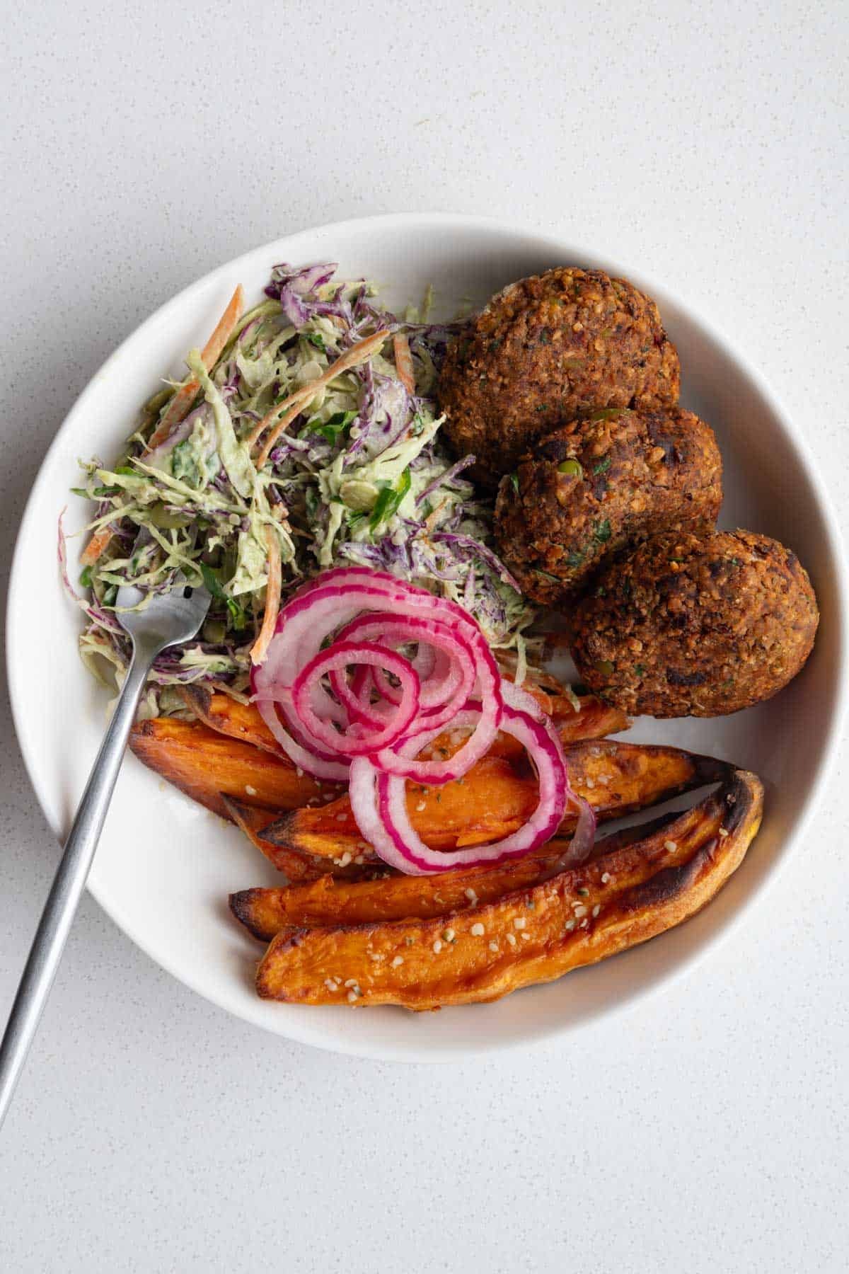 Edamame black bean burgers with pickled red onion, sweet potatoes, and creamy coleslaw in a bowl.