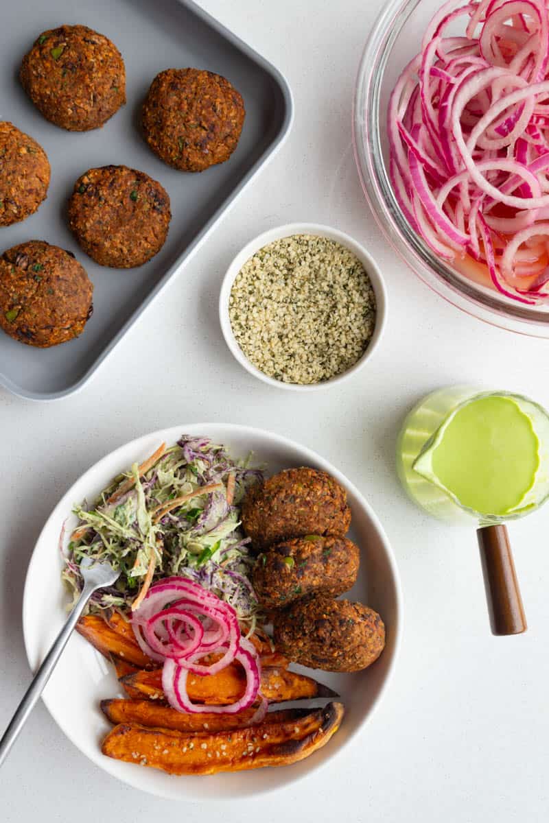 Edamame black bean burgers with pickled red onion, sweet potatoes, creamy coleslaw, green goddess dressing, and hemp hearts.