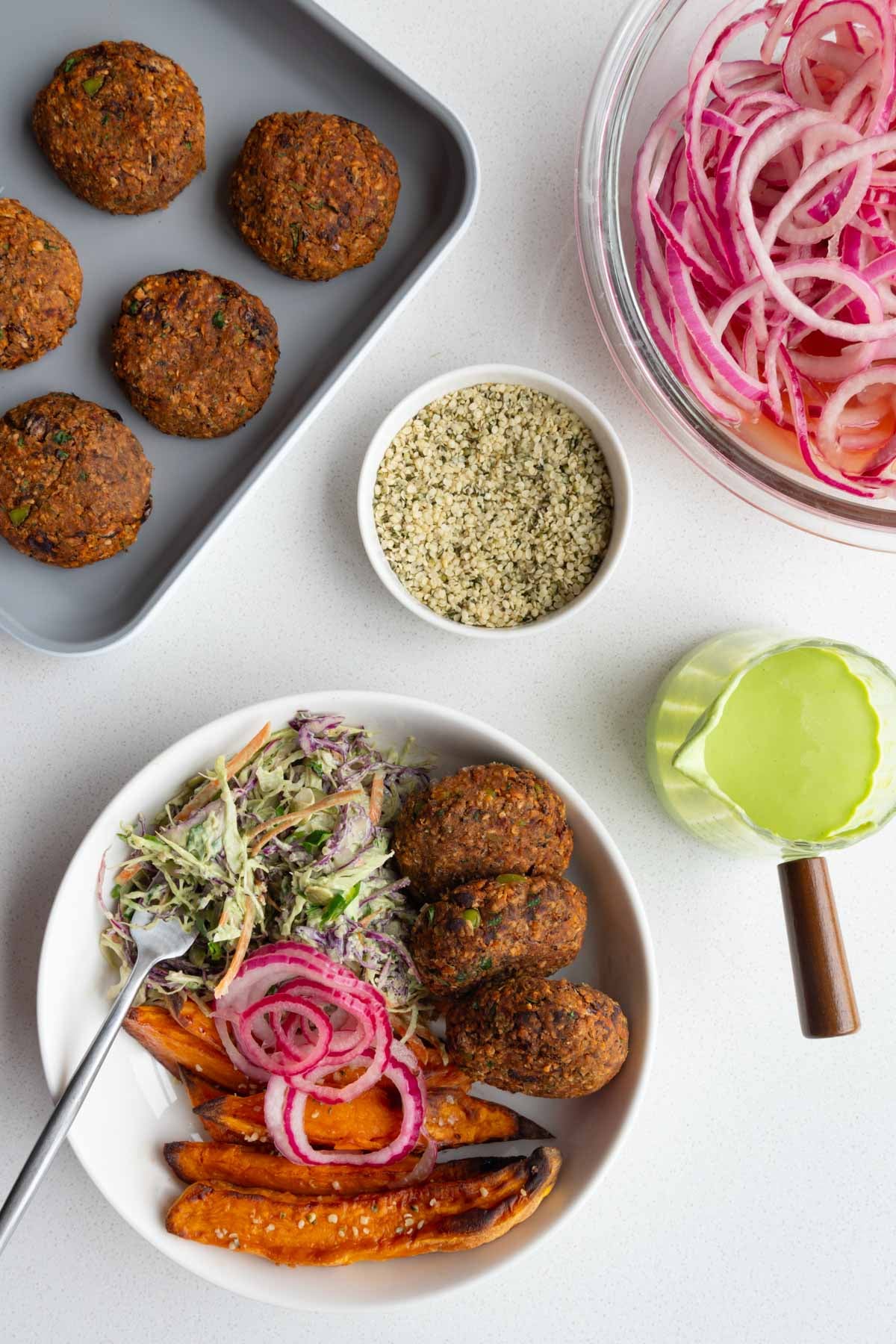 Edamame black bean burgers with pickled red onion, sweet potatoes, creamy coleslaw, green goddess dressing, and hemp hearts.