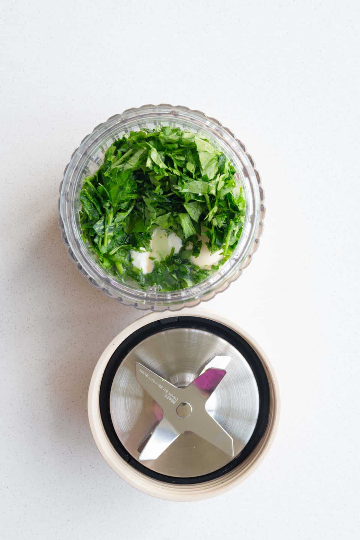 Cilantro, parsley, garlic, lemon juice, tahini, and Greek-style yogurt in the canister of a blender.