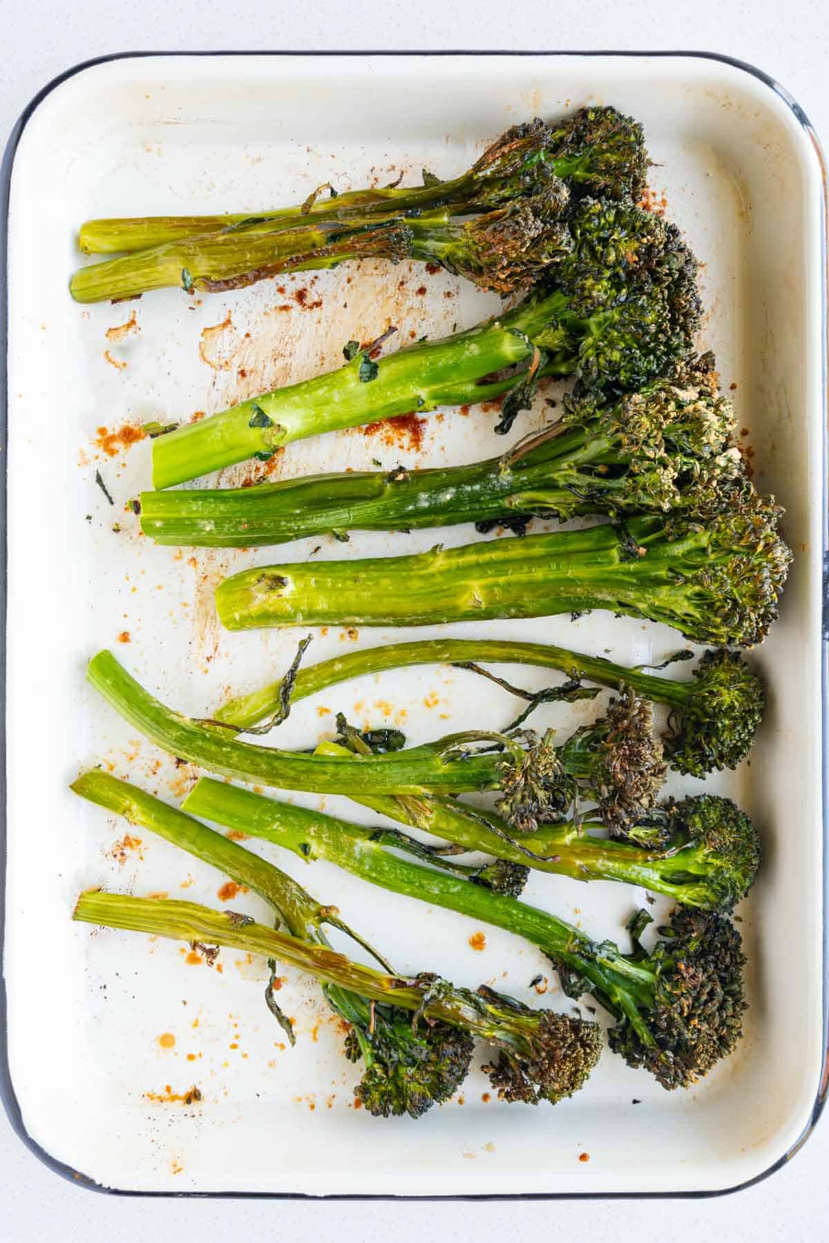 Roasted broccolini on a white baking sheet.