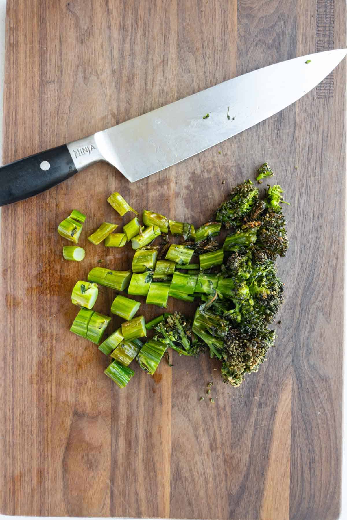 Chopped and roasted broccolini on a wooden cutting board.