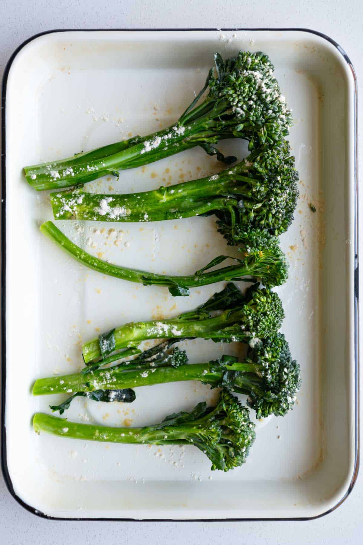 Raw broccolini on a white baking sheet.