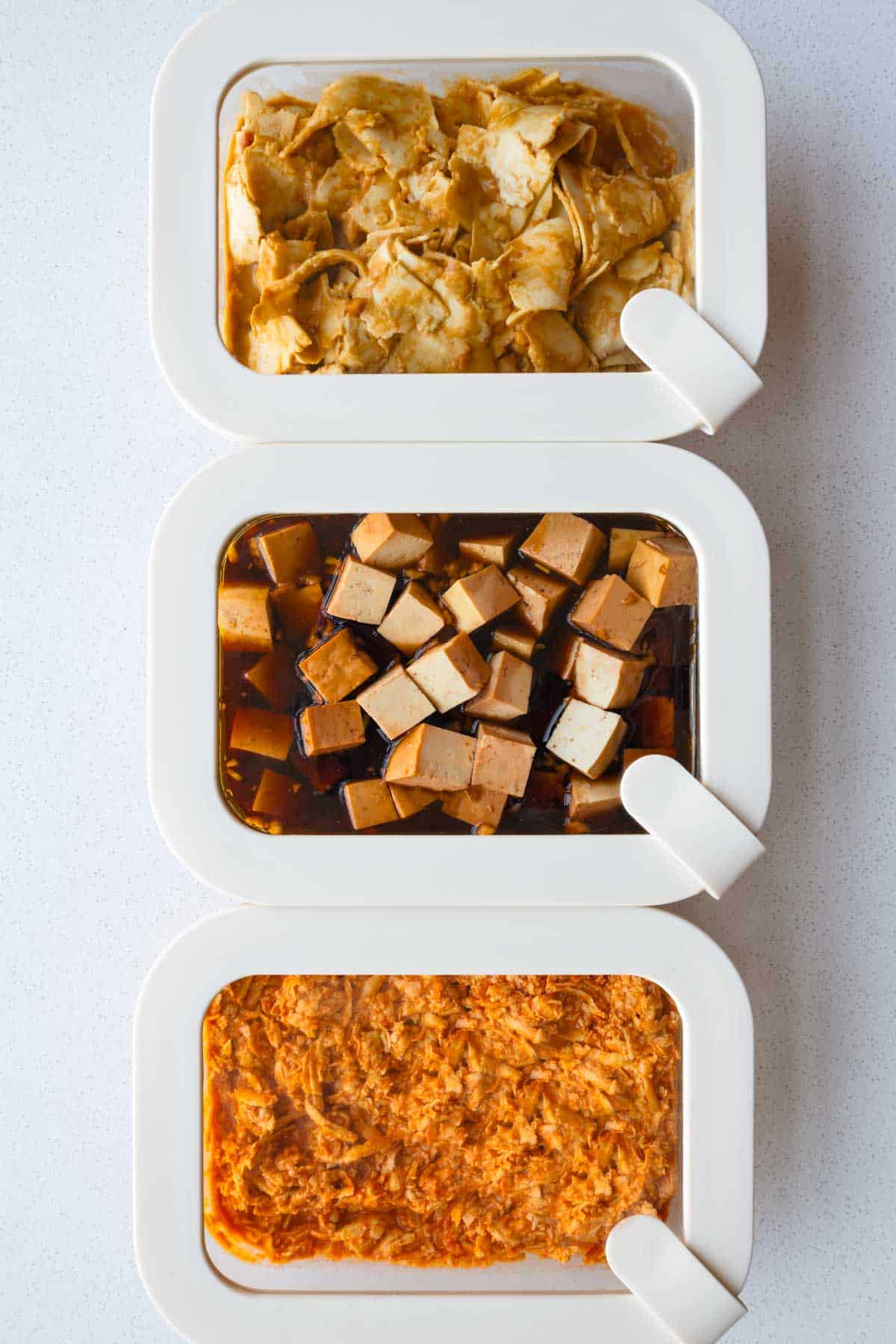 Three tofu marinades in meal prep containers with grated tofu, cubed tofu, and thinly sliced tofu.