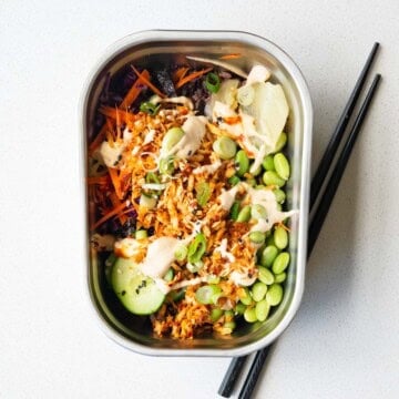 Vegan sushi bowl with cabbage, carrot, cucumber, edamame, 7-grain blend, seaweed, pickled ginger, sesame seeds, scallions, baked grated tofu, and sushi sauce.