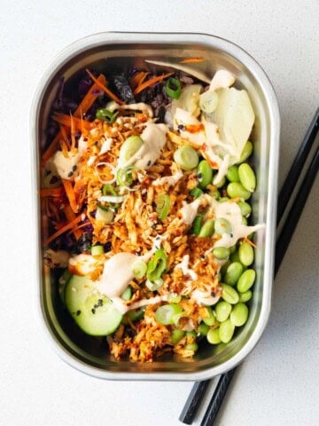 Vegan sushi bowl with cabbage, carrot, cucumber, edamame, 7-grain blend, seaweed, pickled ginger, sesame seeds, scallions, baked grated tofu, and sushi sauce.