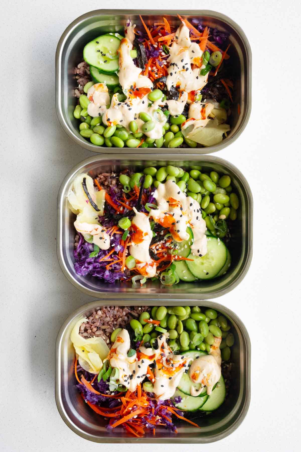 Vegan sushi bowl with cabbage, carrot, cucumber, edamame, 7-grain blend, seaweed, pickled ginger, sesame seeds, scallions, and sushi sauce.