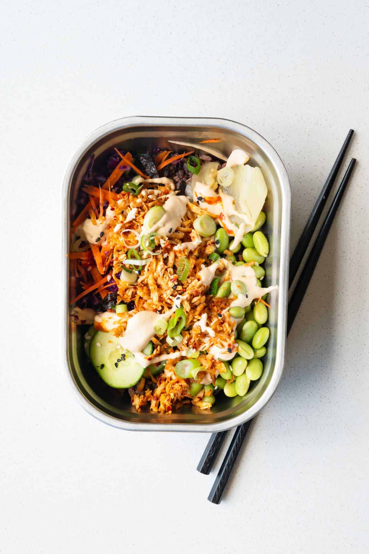 Vegan sushi bowl with cabbage, carrot, cucumber, edamame, 7-grain blend, seaweed, pickled ginger, sesame seeds, scallions, baked grated tofu, and sushi sauce.