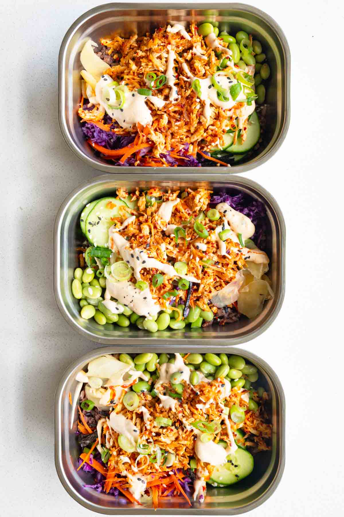 Vegan sushi bowl with cabbage, carrot, cucumber, edamame, 7-grain blend, seaweed, pickled ginger, sesame seeds, scallions, baked grated tofu, and sushi sauce.