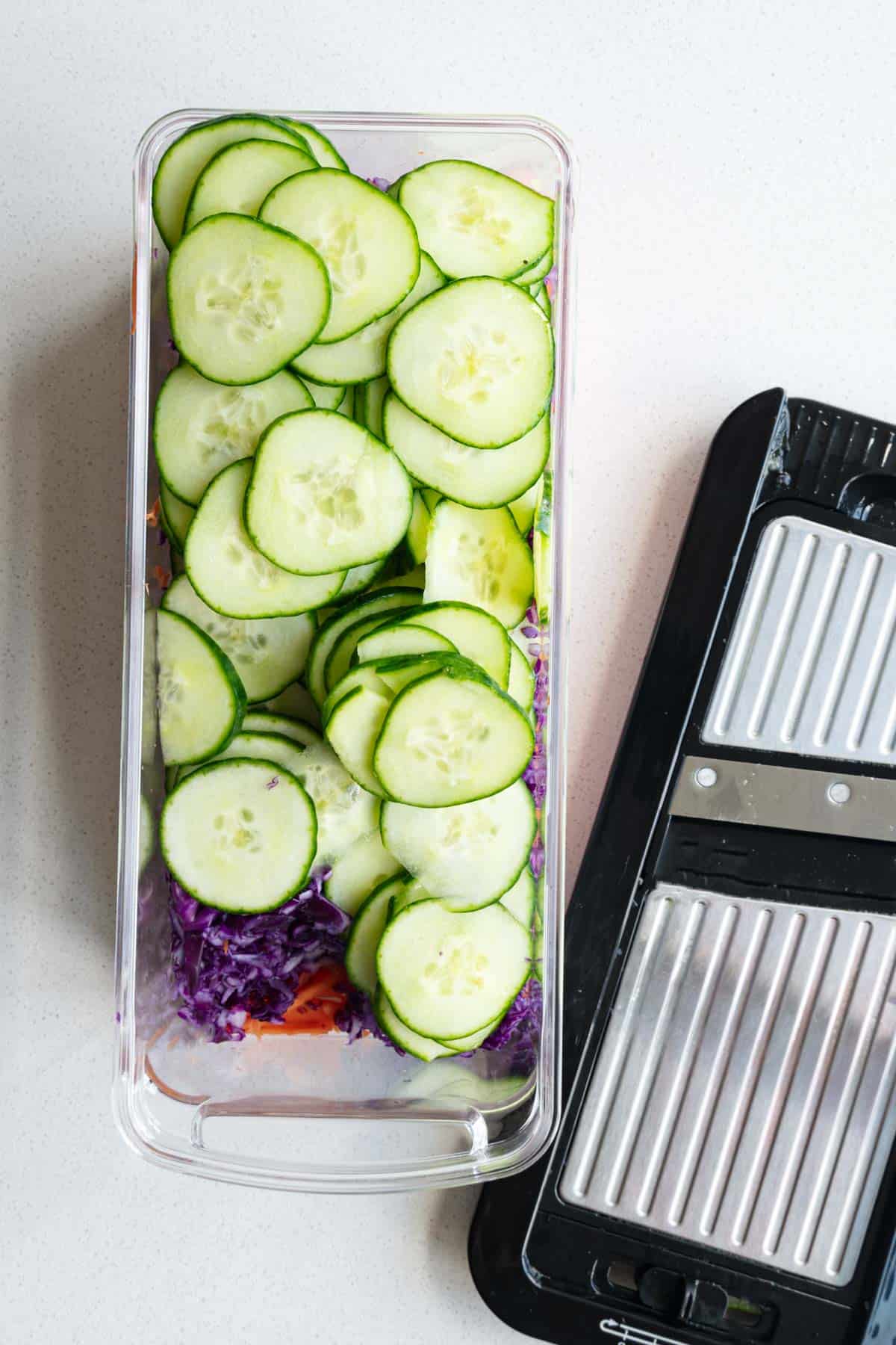 Sliced cucumber, grated red cabbage, and julienned carrots in a veggie chopper.