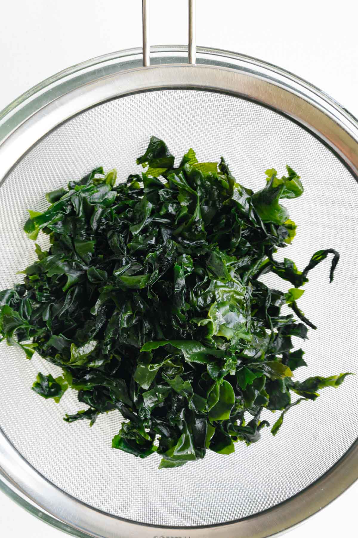 Soaked wakame seaweed in a mesh sieve.