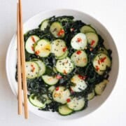 Wakame seaweed salad with cucumber in a white bowl with chopsticks.