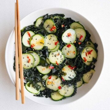 Wakame seaweed salad with cucumber in a white bowl with chopsticks.