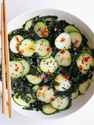 Wakame seaweed salad with cucumber in a white bowl with chopsticks.