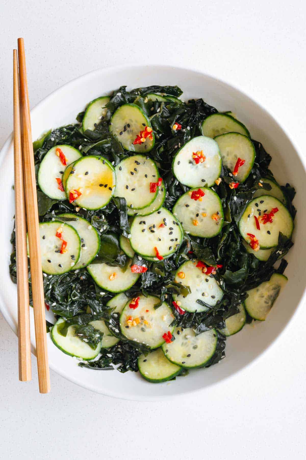 Wakame seaweed salad with cucumber in a white bowl with chopsticks.