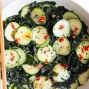Wakame seaweed salad with cucumber in a bowl with chopsticks.