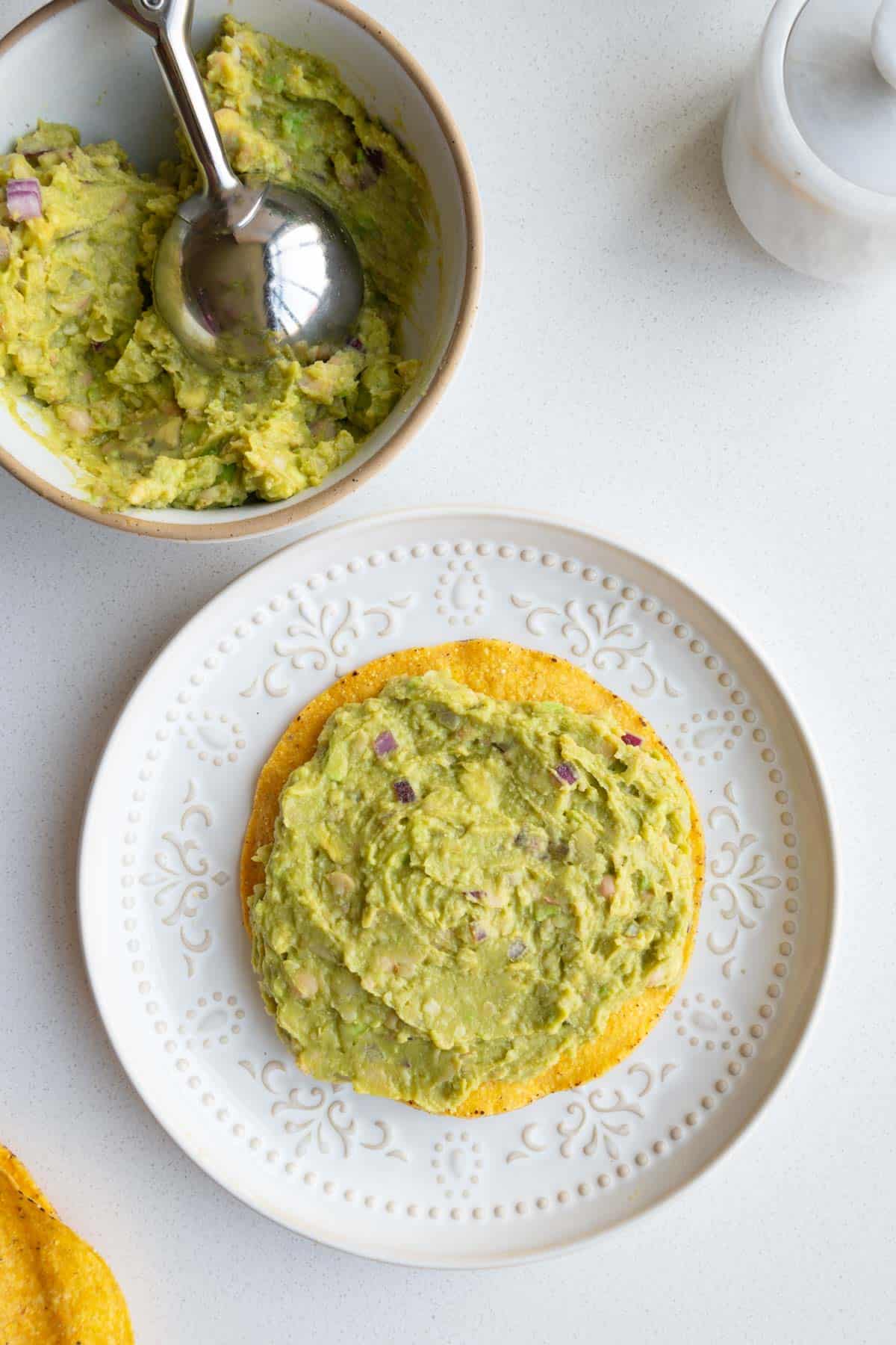 White bean mash in a bowl with an ice cream scoop and on a tostada topped with sprouts.