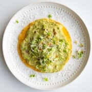 White bean mash with avocado on a tostada topped with sprouts.