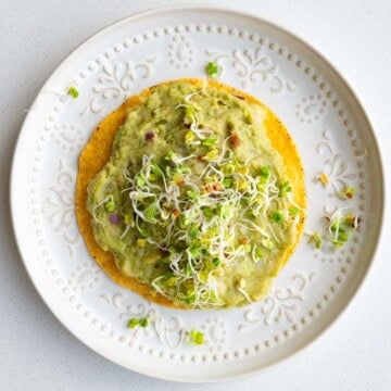 White bean mash with avocado on a tostada topped with sprouts.