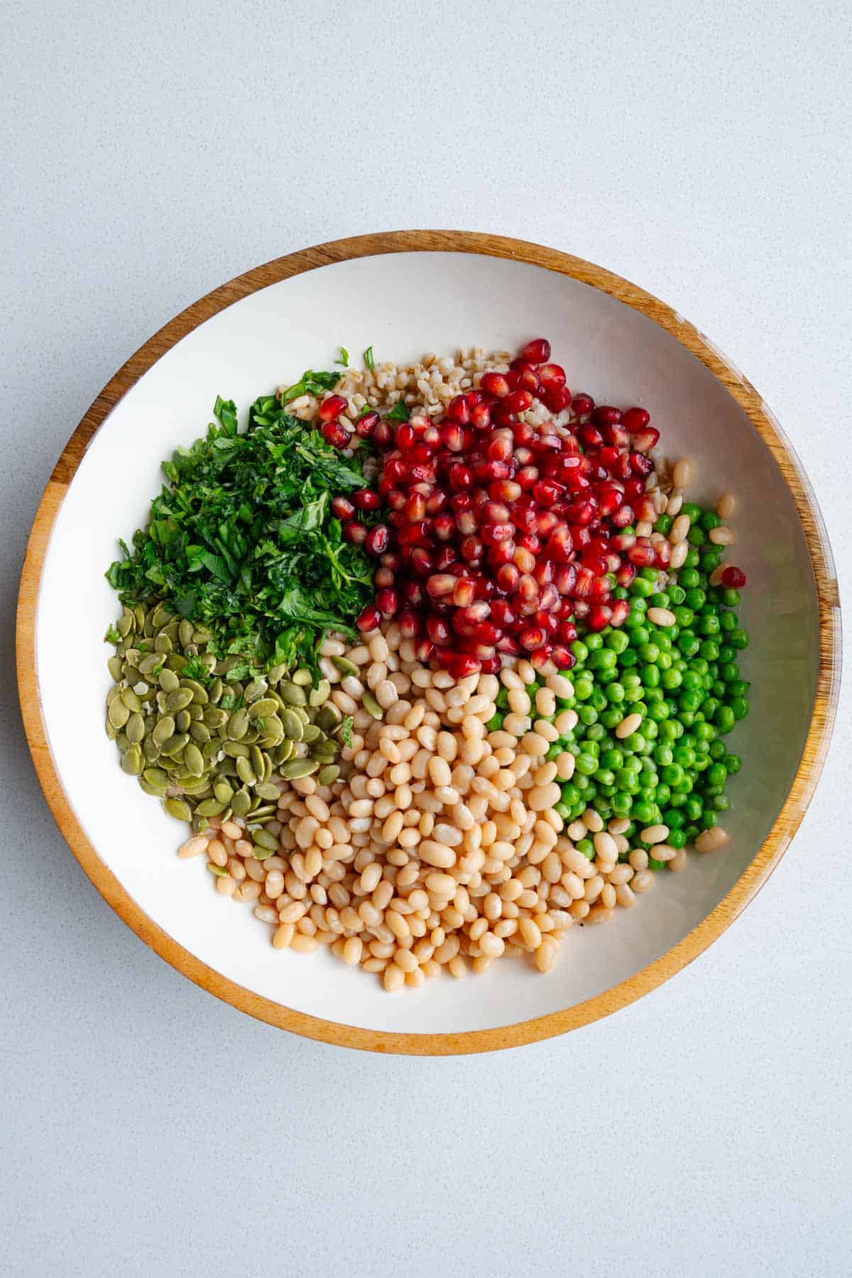 Hulless barley, pomegranate, green peas, pumpkin seeds, and white beans in a bowl.