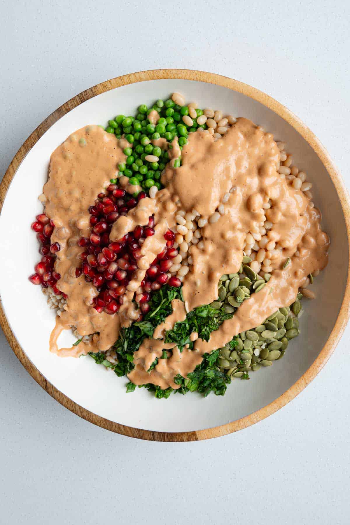 Artichoke dressing with hulless barley, pomegranate, green peas, pumpkin seeds, and white beans in a bowl.