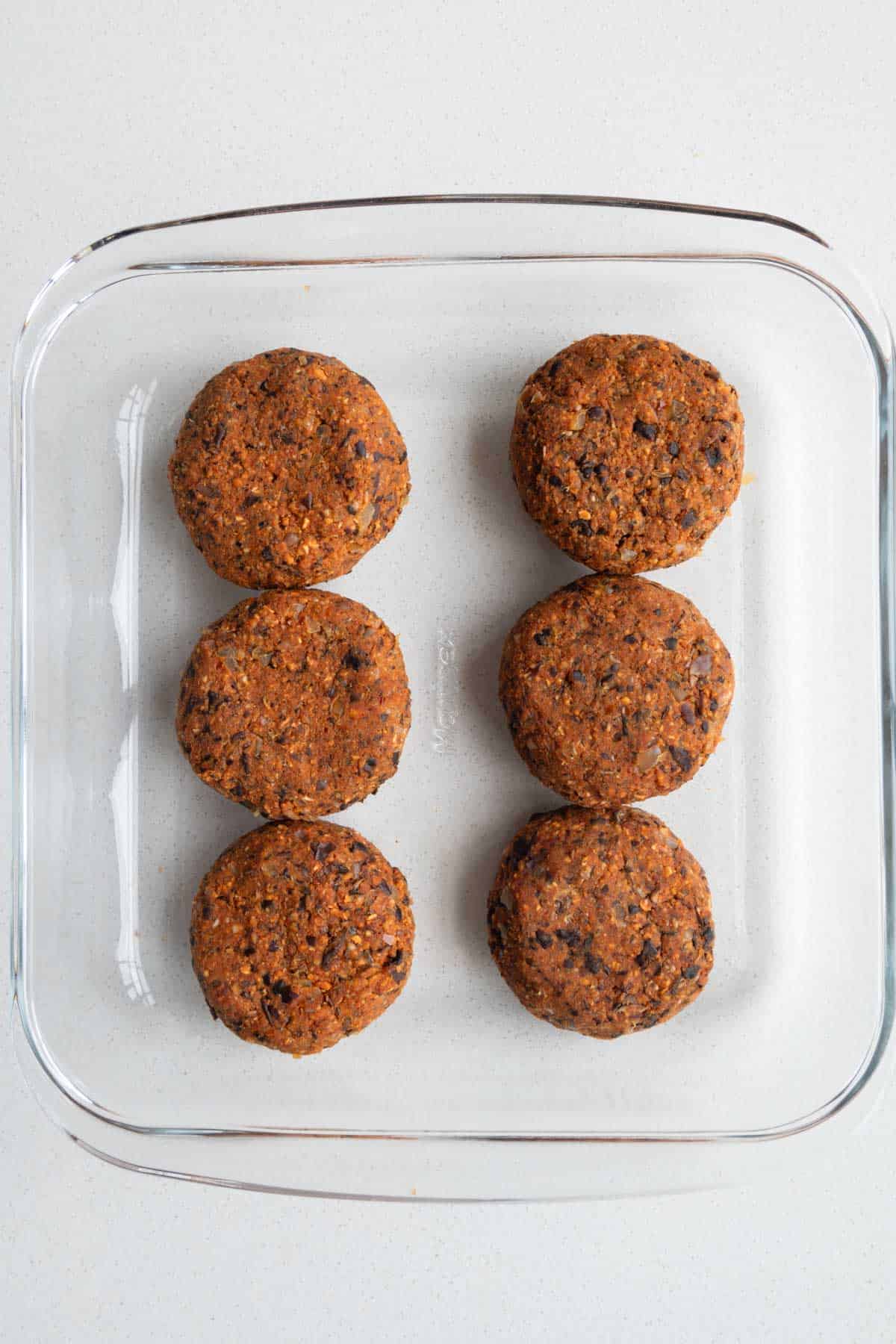 Six formed patties in a glass storage dish.