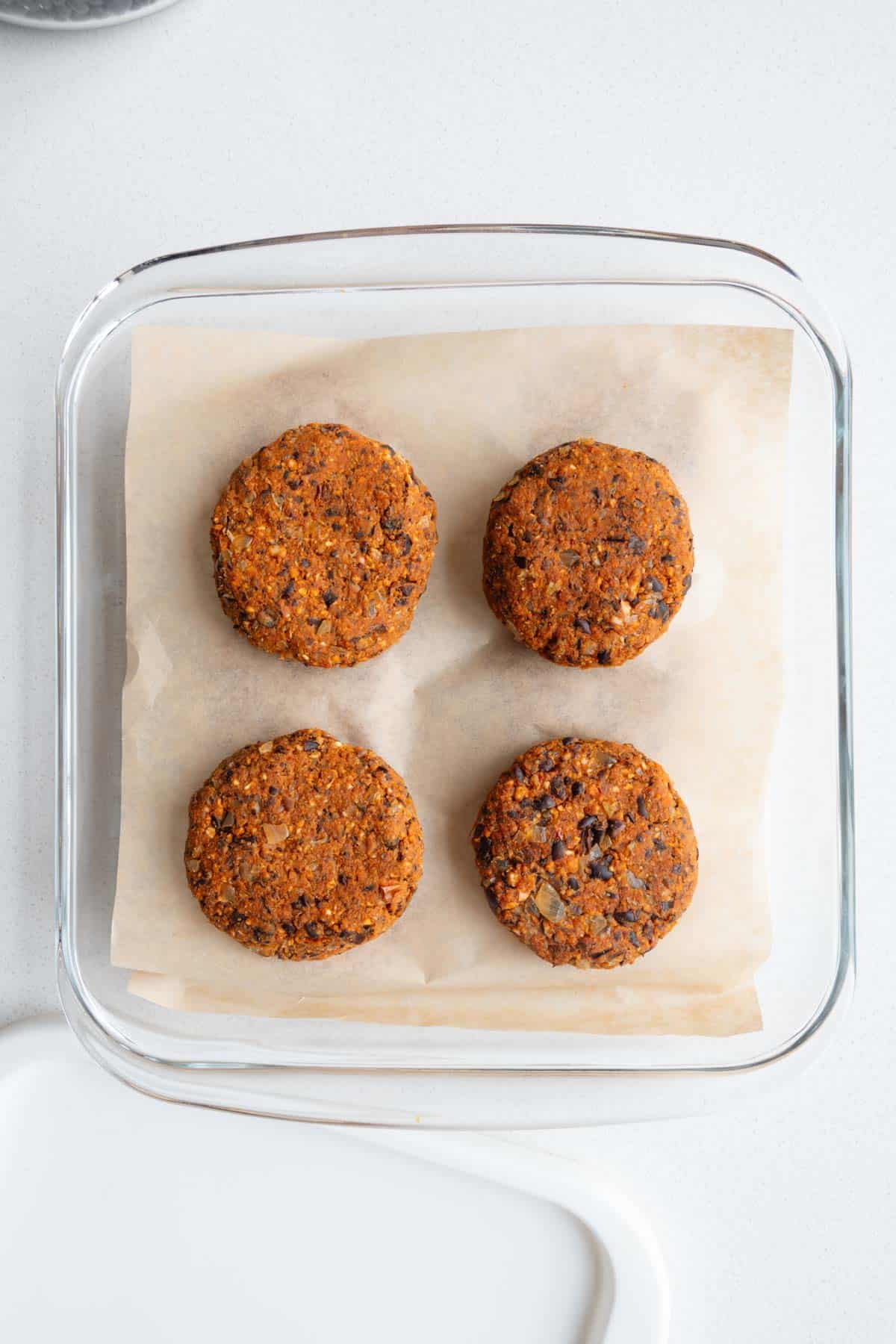 Four formed patties on parchment paper layered for freezing.