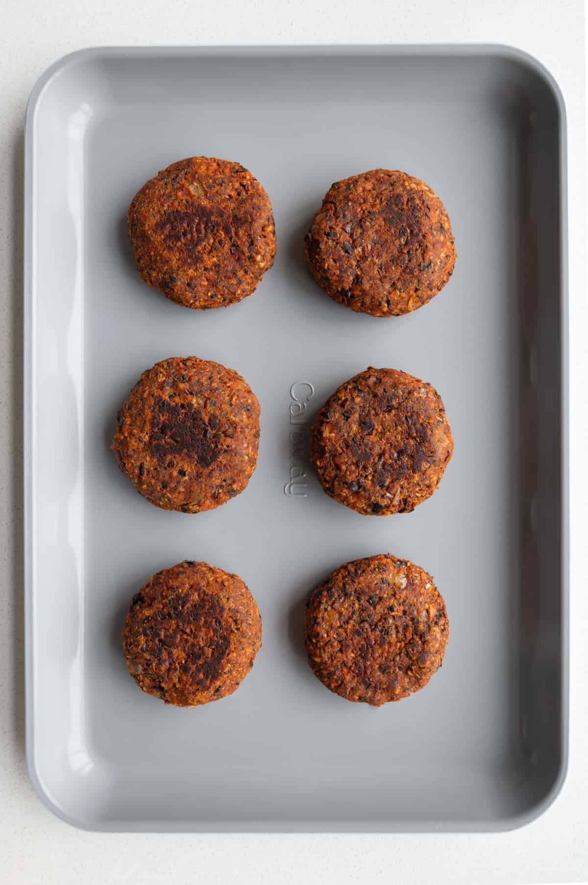 Six baked black soybean burgers on a baking sheet.