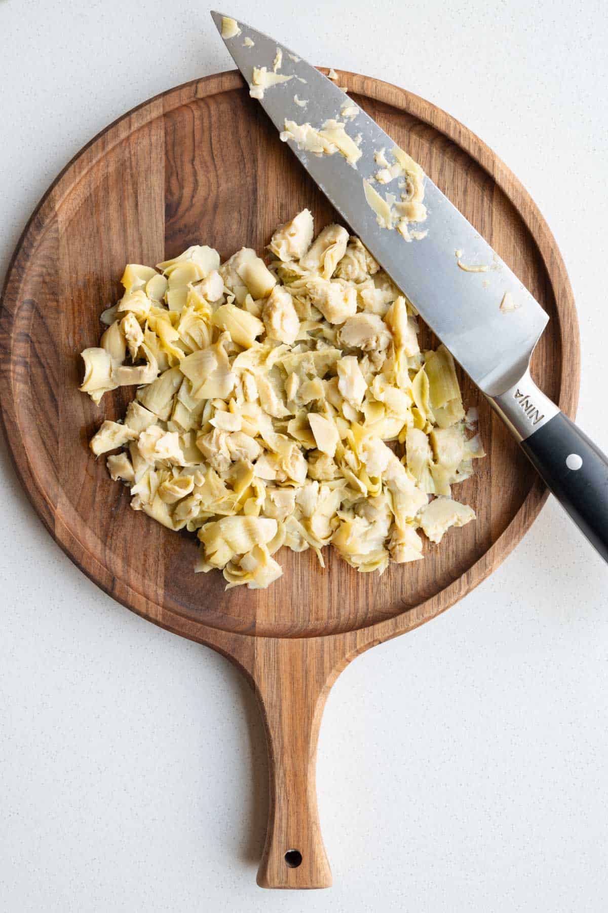 Chopped artichoke hearts on a wooden cutting board.