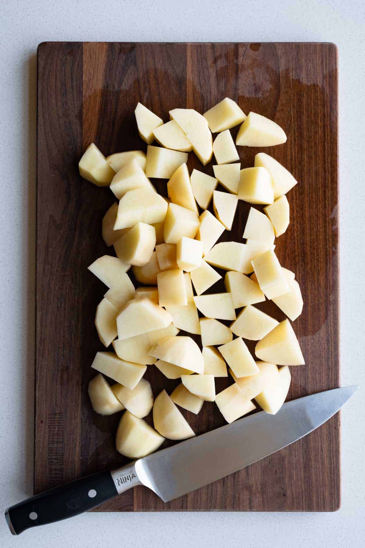 Chopped cooked potatoes on a wooden cutting board.