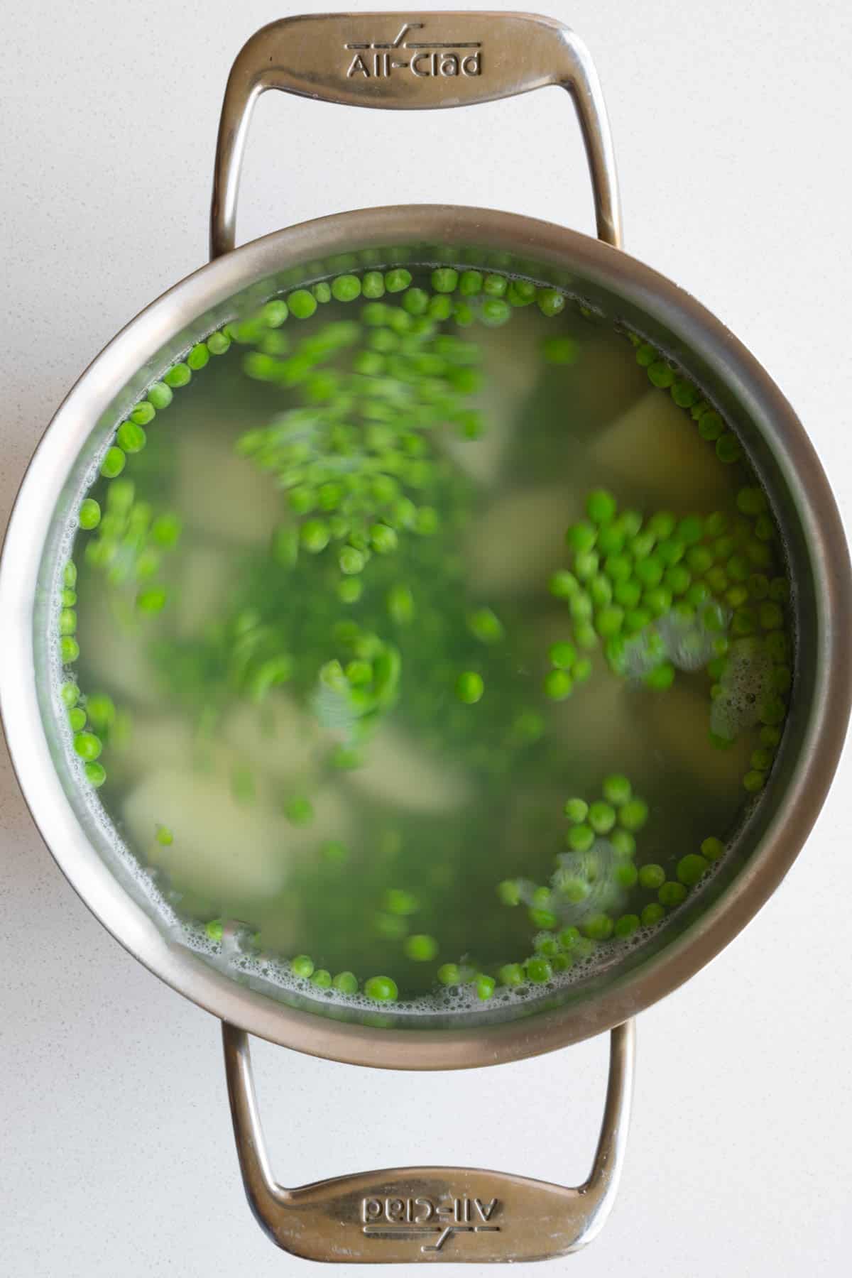 Cooked green peans and potato in water in a saucepan.
